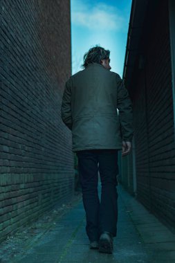 Karanlık şehir sokaklarında yürüyen bir adam. Arka görünüm.