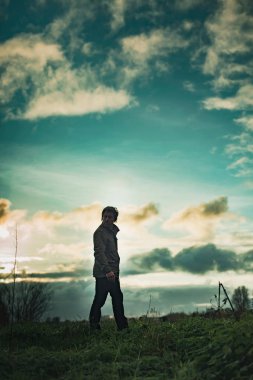 Mysterious man in rural landscape with cloudy sky at sunset. clipart