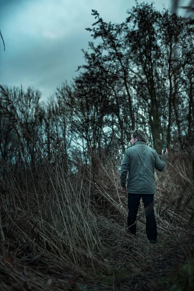 Man with pistol between reed on cloudy day. — Stock Photo, Image