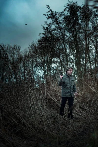 Man met pistool tussen riet op bewolkte dag. — Stockfoto