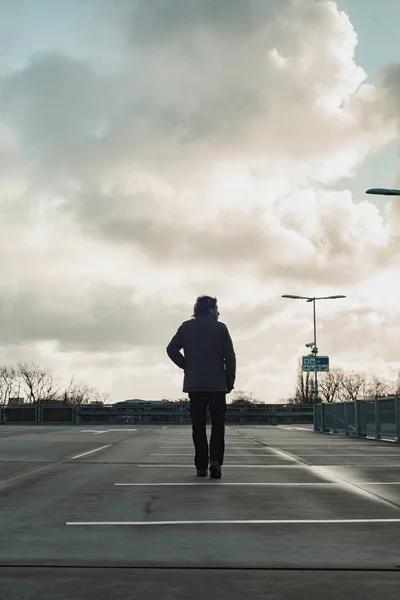 Homme inspectant parking avec ciel nuageux. Vue arrière . — Photo