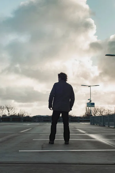 Homme inspectant parking avec ciel nuageux. Vue arrière . — Photo