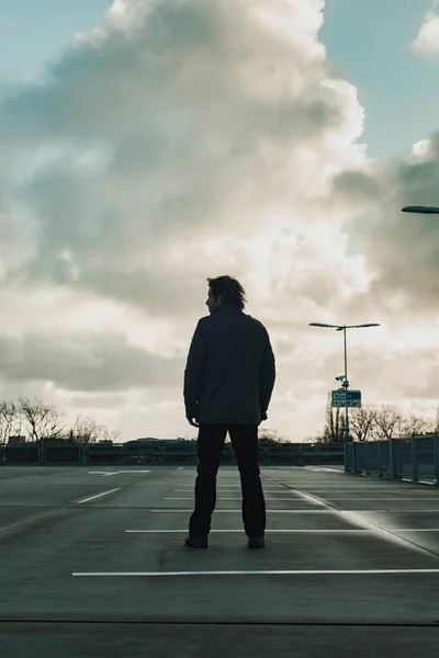 Homme inspectant parking avec ciel nuageux. Vue arrière . — Photo