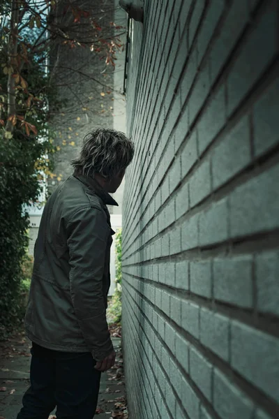 Homme se faufilant le long du mur de briques blanches dans l'allée. Vue arrière . — Photo