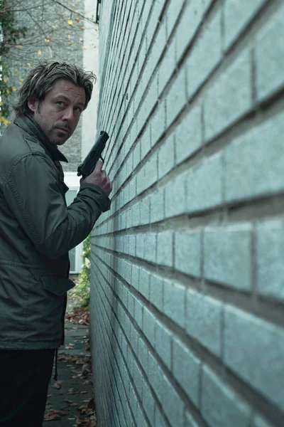 Man with pistol in alley along white brick wall. — Stock Photo, Image