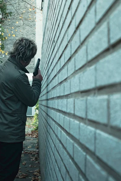 Man with pistol in alley along white brick wall. Rear view. — Stock Photo, Image