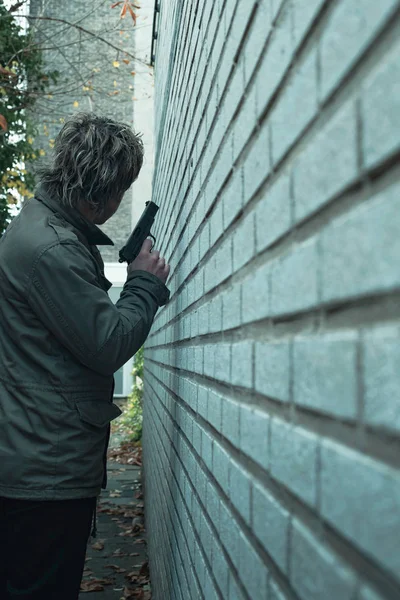 Man with pistol in alley along white brick wall. Rear view. — Stock Photo, Image