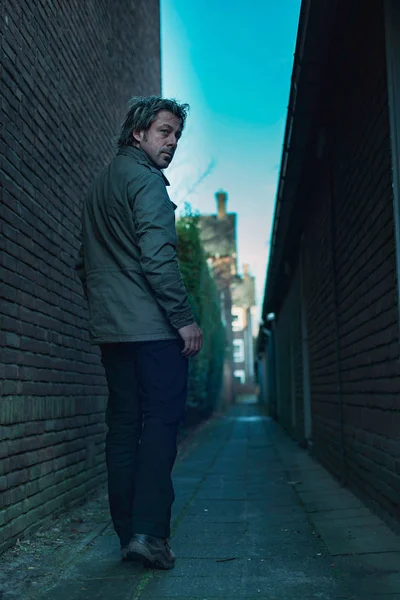 Man walking in dark urban alley. Looking over shoulder. Rear vie — Stockfoto