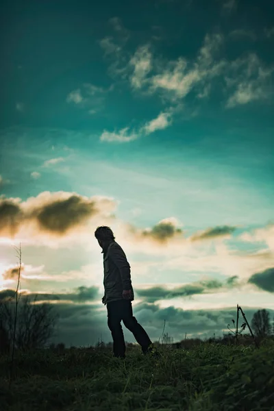 Homme mystérieux dans un paysage rural avec un ciel nuageux au coucher du soleil . — Photo