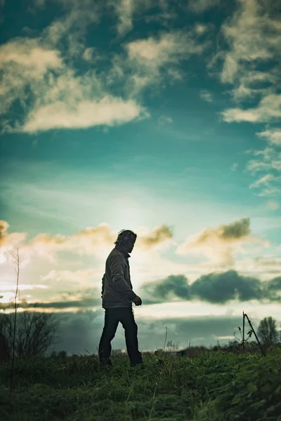 Homme mystérieux dans un paysage rural avec un ciel nuageux au coucher du soleil . — Photo