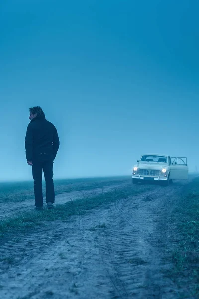 Man in black jacket and trousers with classic car on muddy count — Stock Photo, Image