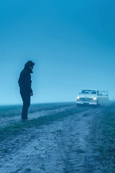 Мужчина в черной куртке и брюках с классической машиной на грязном счету — стоковое фото