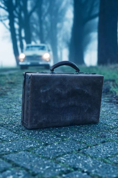 Starý kufřík na venkovské silnici za mlhavého soumraku s klasickým autem — Stock fotografie