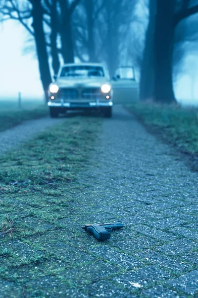 Pistola caiu na estrada rural durante o crepúsculo nebuloso com ca clássico — Fotografia de Stock