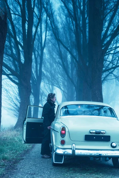Homem de casaco preto e calças em pé à porta do carro clássico — Fotografia de Stock