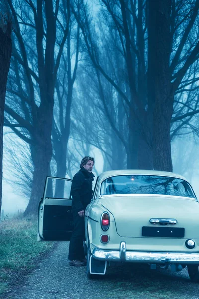 Man in black jacket and trousers standing at door of classic car — Stock Photo, Image