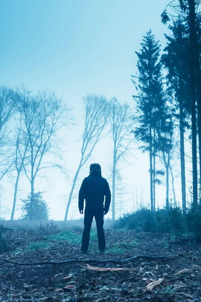 Hombre de chaqueta negra y pantalones en el bosque de invierno brumoso . — Foto de Stock