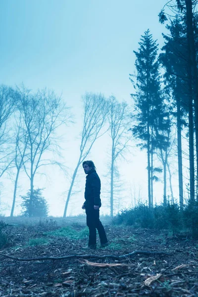 Homem de casaco preto e calças na floresta nebulosa de inverno . — Fotografia de Stock