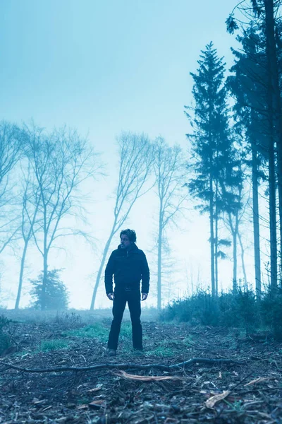 Hombre de chaqueta negra y pantalones en el bosque de invierno brumoso . — Foto de Stock