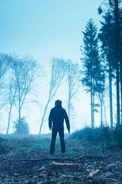 Férfi fekete dzsekiben fegyverrel ködös téli erdőben. — Stock Fotó