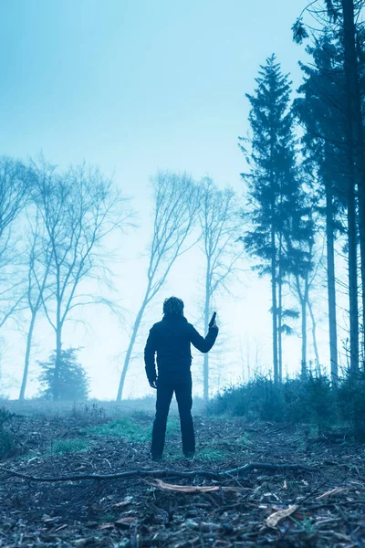 Homem de casaco preto com arma na floresta nebulosa de inverno . — Fotografia de Stock