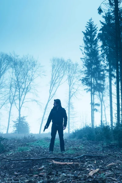 Man in black jacket with gun in foggy δάσος χειμώνα. — Φωτογραφία Αρχείου