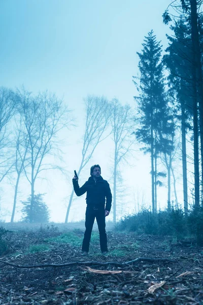 Homem de casaco preto com arma na floresta nebulosa de inverno . — Fotografia de Stock