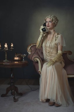 1920 'lerin moda kadını koltukta otururken telefonla konuşuyor.