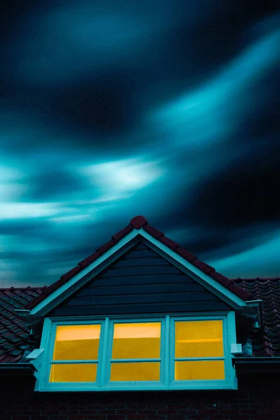 Casa misteriosa con ventana iluminada bajo el cielo tormentoso al atardecer . — Foto de Stock