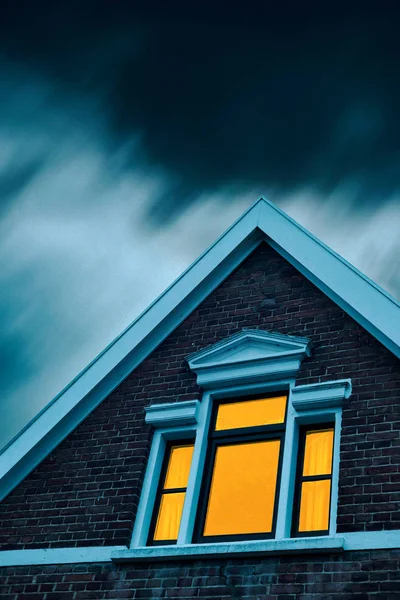 Casa inquietante con finestra illuminata sotto il cielo tempestoso al tramonto . — Foto Stock