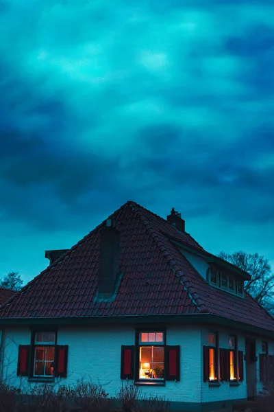 Creepy house with illuminated windows under stormy sky at twilig