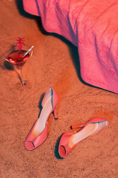 Rosa vintage scarpe da donna e bicchiere da cocktail in sabbia accanto al sole — Foto Stock