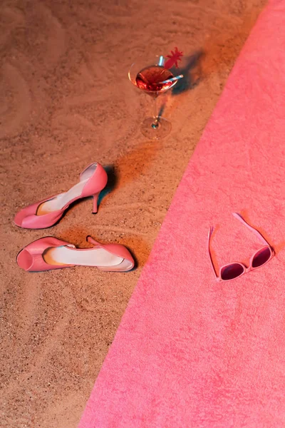 Vintage ladies shoes and cocktail glass in sand next to pink tow