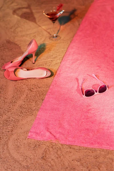 Vintage ladies shoes and cocktail glass in sand next to pink tow — Stockfoto