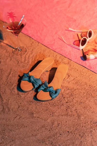 Vintage ladies shoes and cocktail glass in sand next to pink tow — Stock Photo, Image