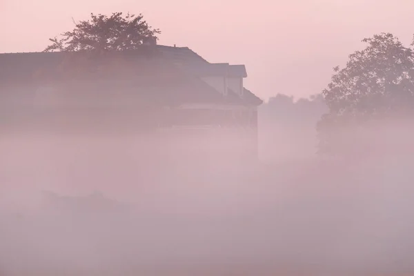 Starý statek v zamlžené krajině při východu slunce. — Stock fotografie