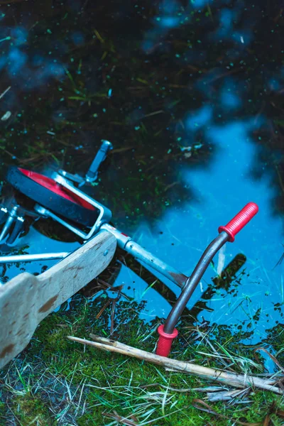 Abandoned kids tricycle in puddle of dark water in forest. — Stock Photo, Image