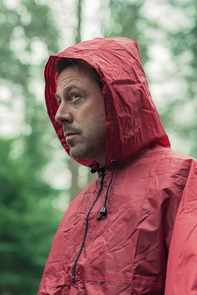 Man in red hooded raincoat in forest.