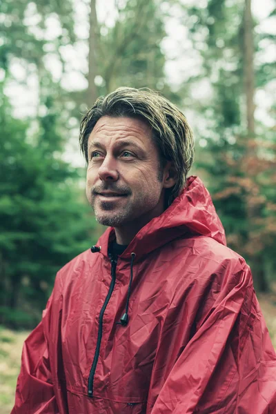 Smiling man in red raincoat in woods.