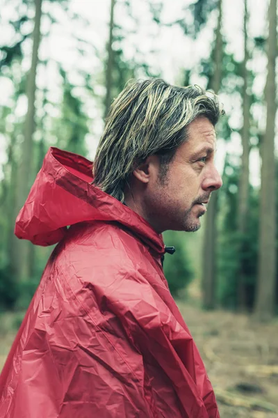 Man in red raincoat in forest. Side view. — Stock Photo, Image