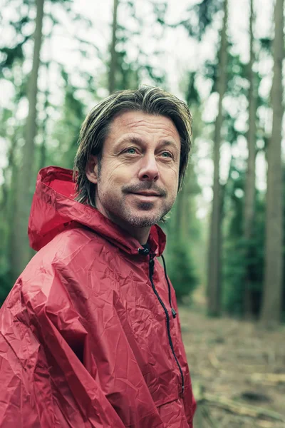 Glimlachende man in rode regenjas in het bos. — Stockfoto