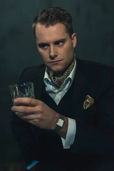 Retro moda człowiek w ciemnym garniturze posiada szklankę whisky. — Zdjęcie stockowe