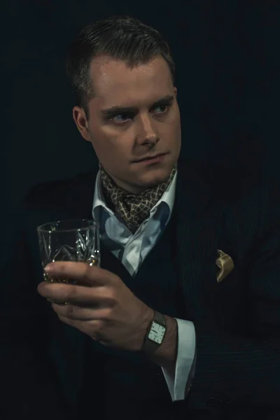 Retro fashion man in dark suit holds a glass of whiskey. — Stok fotoğraf