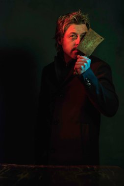 Man holding meat cleaver in front of face. Standing in red and g