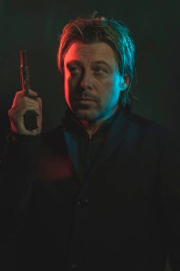 Man holding pistol next to his head. Illminated by red and blue 