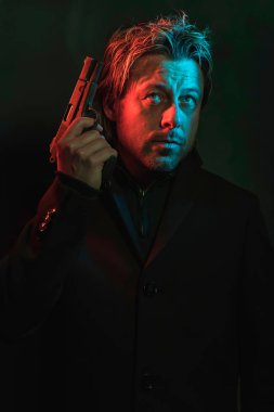 Man holding pistol next to his head. Illminated by red and blue 