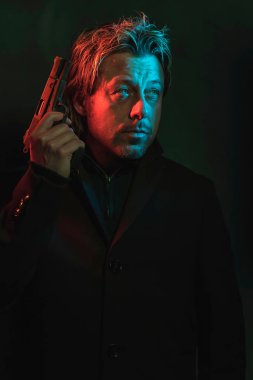 Man holding pistol next to his head. Illminated by red and blue 