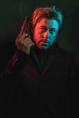 Man holding pistol next to his head. Illminated by red and blue 