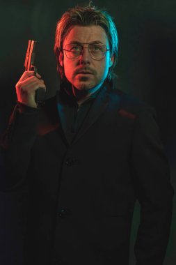 Man holding gun next to his head. Illminated by red and blue lig