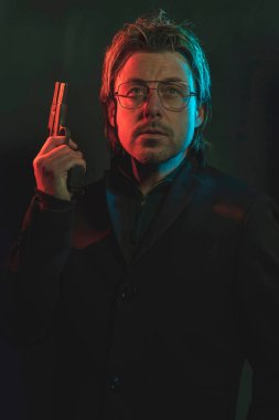 Man holding gun next to his head. Illminated by red and blue lig